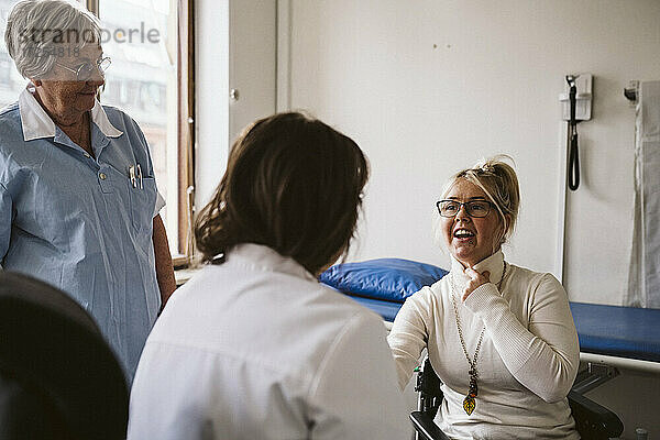 Ältere weibliche Krankenschwester schaut auf eine behinderte Frau  die sich mit einem Arzt in einer medizinischen Klinik berät