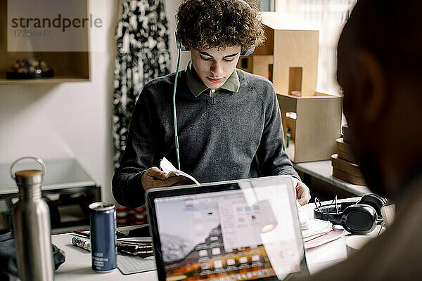 Teenager-Junge studiert  während der Vater am Laptop am Schreibtisch arbeitet