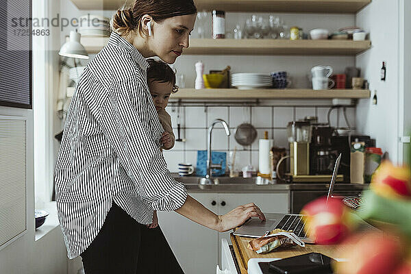 Weibliche Unternehmerin arbeitet am Laptop mit Baby-Junge in der Küche