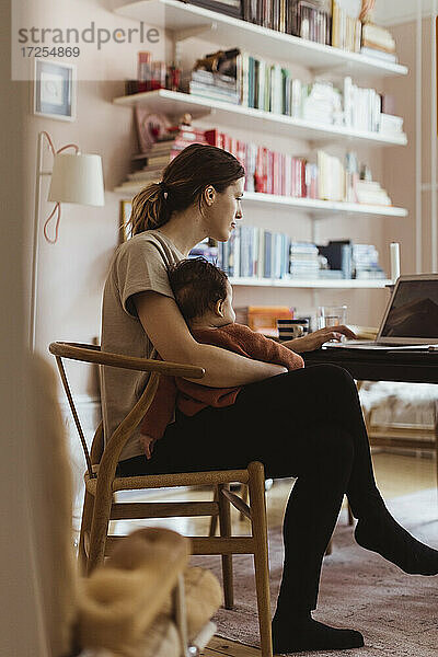 Weibliche professionelle Arbeit am Laptop  während mit Baby Junge im Büro zu Hause sitzen