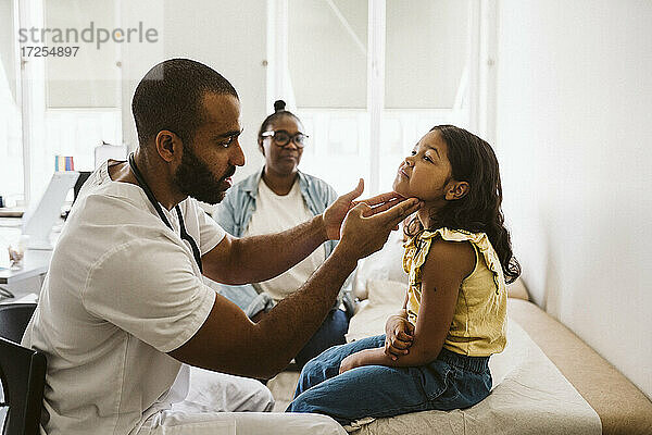 Männlicher Arzt  der den Hals eines Mädchens untersucht  während er in einer medizinischen Klinik sitzt