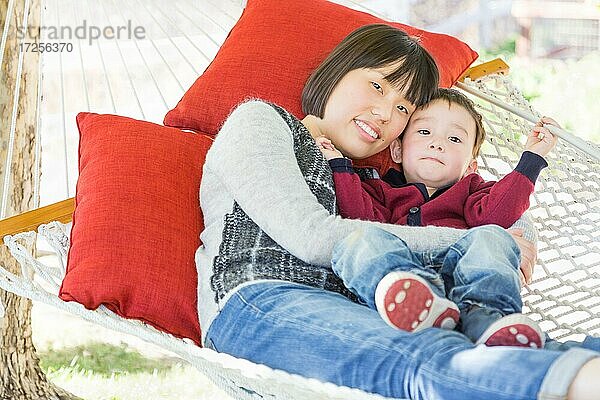 Glückliche chinesische Mutter mit Spaß mit ihrem gemischtrassigen kleinen Sohn in Hängematte im Freien