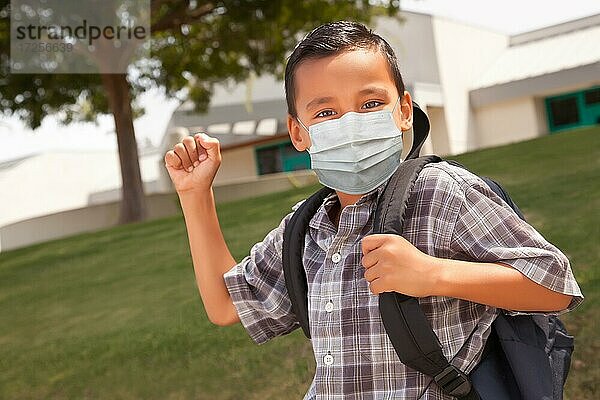 Hispanischer Schüler Junge mit Gesichtsmaske und Rucksack auf dem Schulgelände