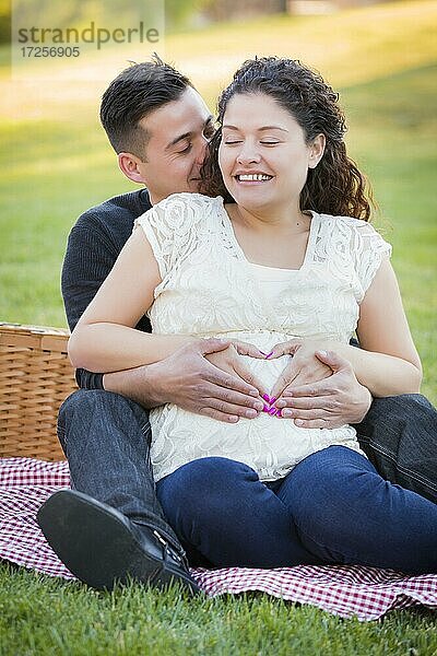 Schwangeres hispanisches Paar machen Herzform mit Händen auf Bauch im Park im Freien