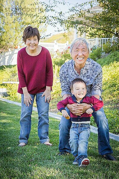 Glückliche chinesische Großeltern haben Spaß mit ihrem gemischtrassigen Enkel draußen