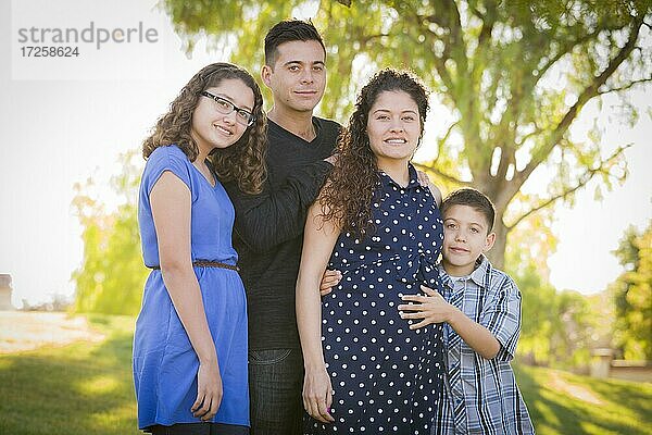 Glückliche attraktive hispanische Familie mit ihrer schwangeren Mutter im Freien im Park