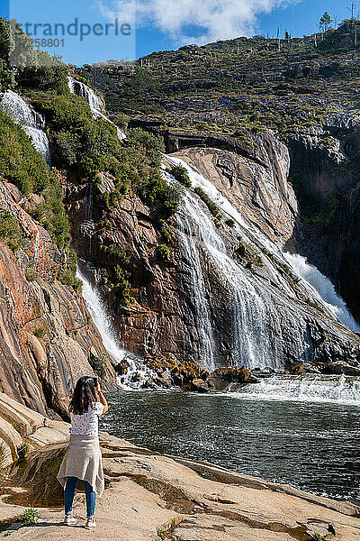 Kaukasische Frau fotografiert Ezaro Wasserfall mit Wasser auf See zwischen Felsen in Galizien  Spanien  Europa stürzt