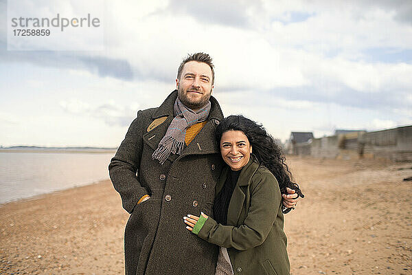 Porträt glücklich zärtliches Paar in Wintermäntel umarmen am Strand