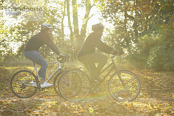 Paar Fahrradfahren durch Herbstblätter in sonnigen Park