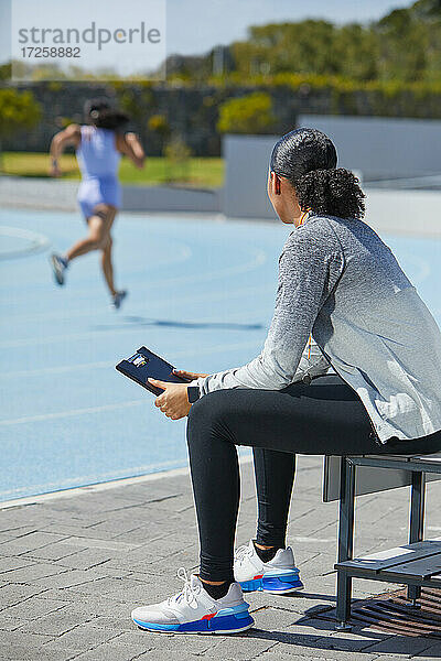 Weiblicher Leichtathletik-Trainer beobachtet Läufer auf sonniger Strecke