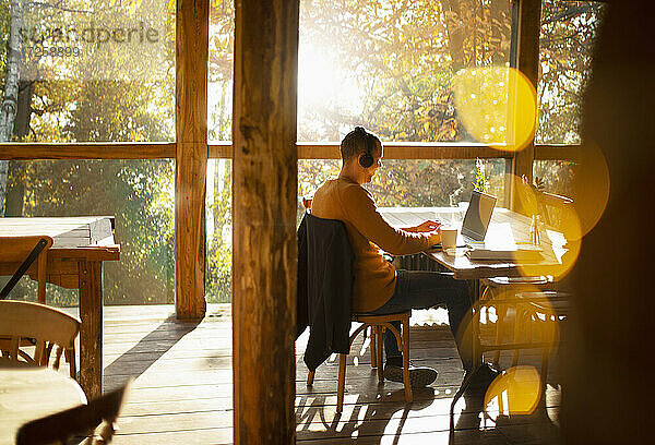 Geschäftsmann mit Kopfhörer arbeiten am Laptop in sonnigen Cafe