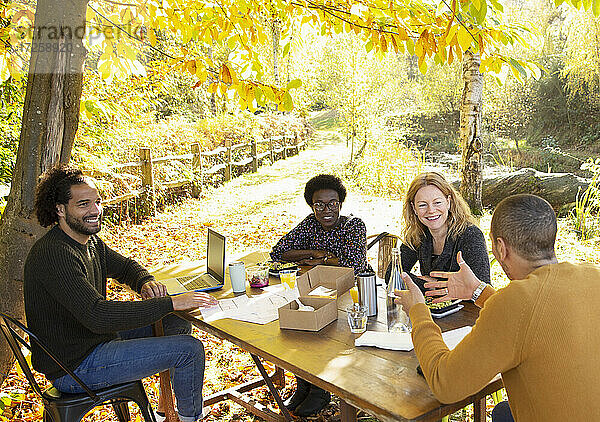 Glückliche Geschäftsleute treffen sich am Tisch im sonnigen Herbst Park