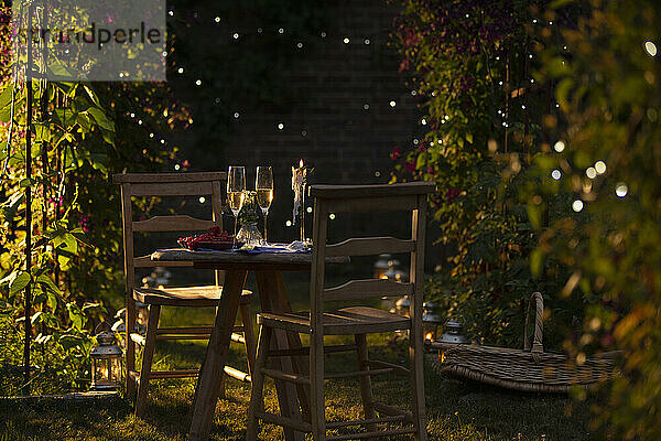 Champagner und rote Johannisbeeren am idyllischen Sommergartentisch bei Sonnenuntergang