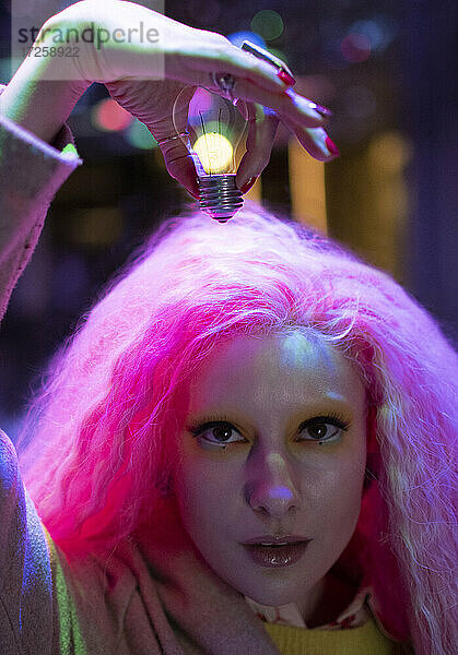 Porträt kühle Frau mit rosa Haar hält Glühbirne über Kopf