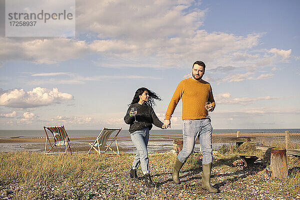 Glückliches Paar mit Wein halten Hände zu Fuß auf sonnigen Strand