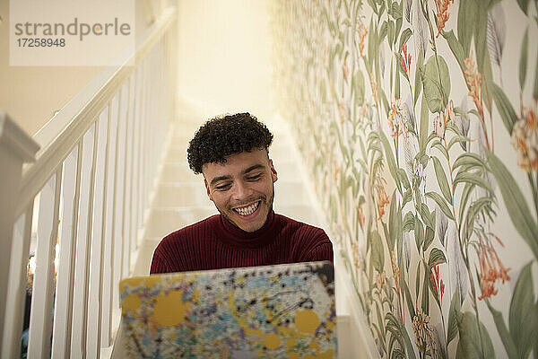 Glücklicher junger Mann mit Laptop auf der Treppe