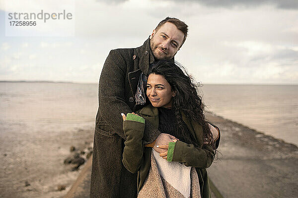 Porträt zärtliches Paar umarmt auf Winter Ozean Steg