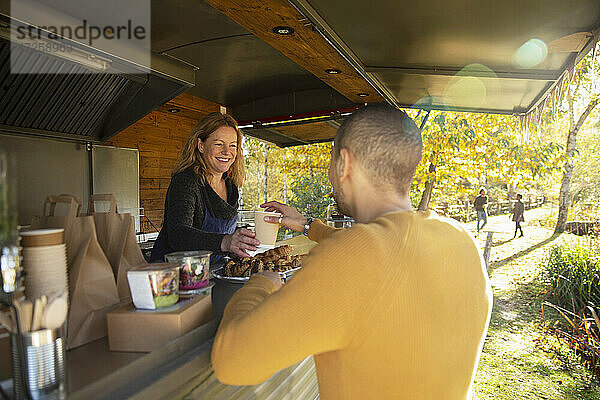 Freundlicher Imbisswagenbesitzer serviert Kaffee an Kunden im Herbstpark