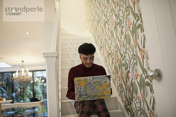 Junger Mann mit Laptop auf Wohnungstreppe