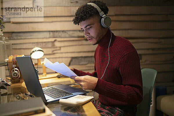 Junger Mann mit Kopfhörer und Papierkram arbeiten spät zu Hause