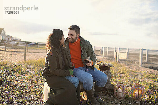 Glückliches romantisches Paar genießt Wein am Feuer auf der Winterstrand-Terrasse