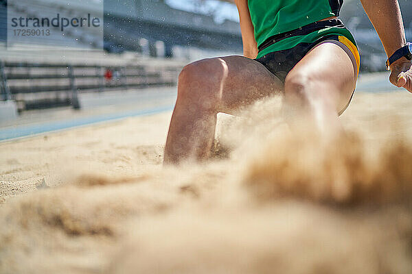 Weiblicher Leichtathletik-Weitspringer bei der Landung im Sand