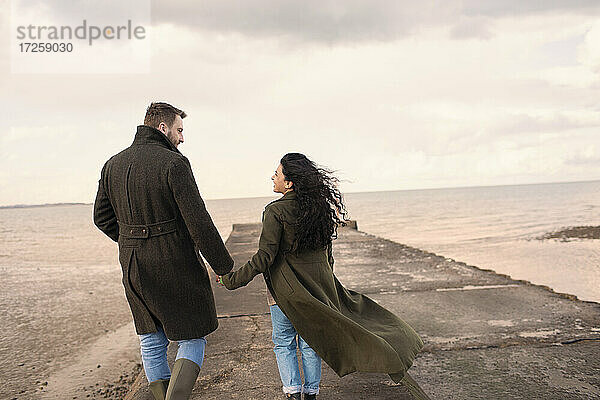 Paar in Wintermäntel halten Hände auf Ozean Strand Steg