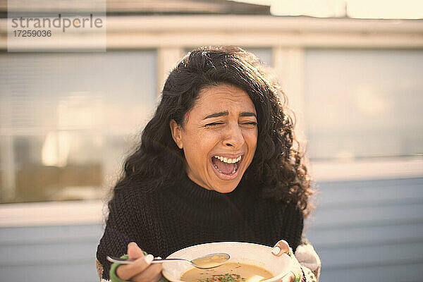Glückliche lachende Frau  die auf einer sonnigen Terrasse Fischsuppe isst