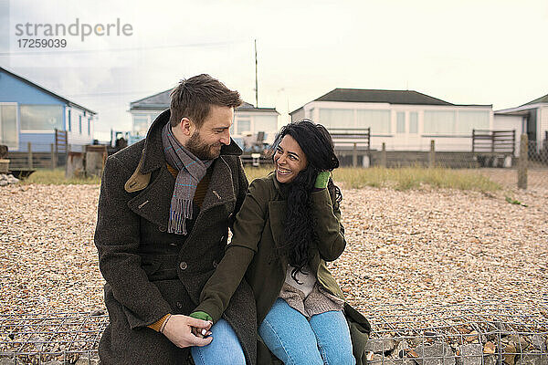 Glückliches Paar in Wintermänteln vor Strandhäusern
