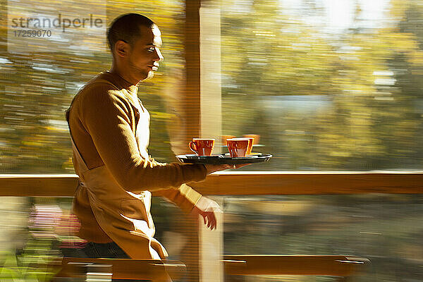 Männliche Barista trägt Tablett von Kaffeetassen entlang Herbst Café Fenster