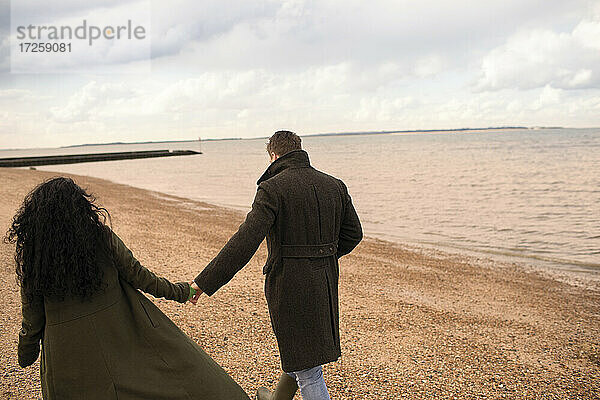Zärtliches Paar  das sich an den Händen hält  geht am Strand des Wintermeeres spazieren