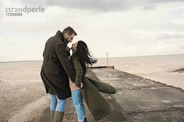 Glücklich liebevolles Paar in Wintermäntel auf Ozean Strand