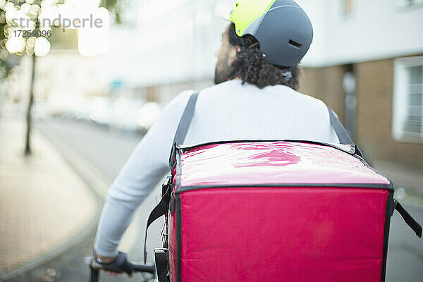 Männlicher Fahrradkurier mit Helm  der Essen auf einer städtischen Straße ausliefert