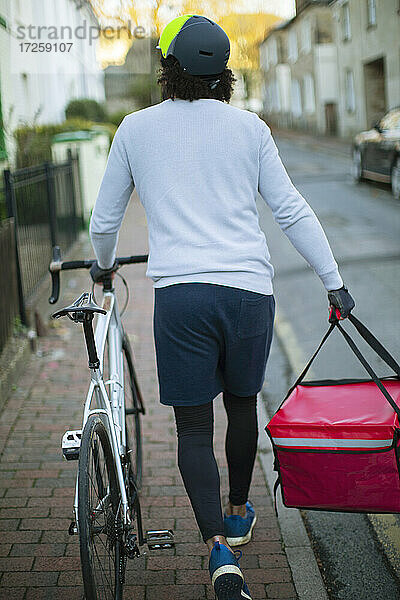 Männlicher Fahrradkurier  der Lebensmittel in einem städtischen Viertel ausliefert