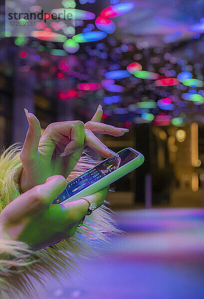 Close up Frau mit Smartphone in Nachtclub unter Neonlicht