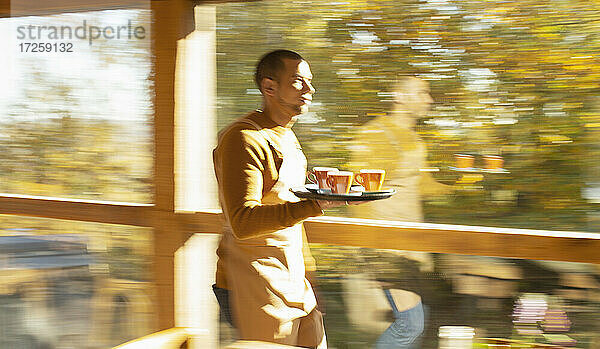 Männliche Barista trägt Tablett mit Kaffee entlang sonnigen Herbst Café Fenster