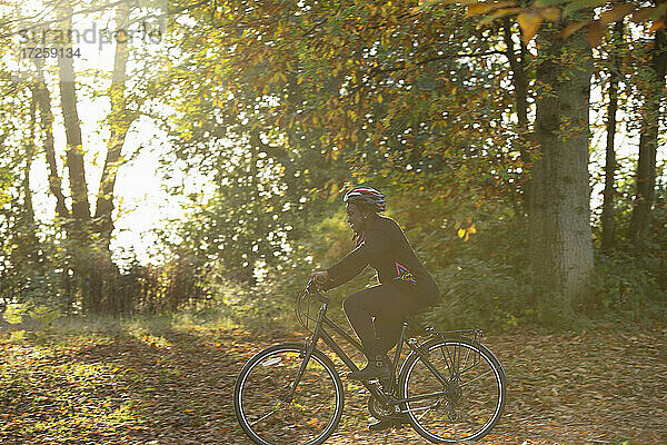 Glückliche Frau Fahrradfahren unter Herbstlaub in sonnigen Park