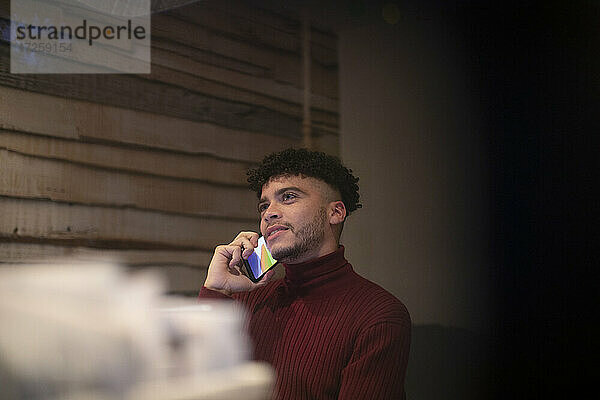 Junger Mann spricht am Smartphone im Home-Office