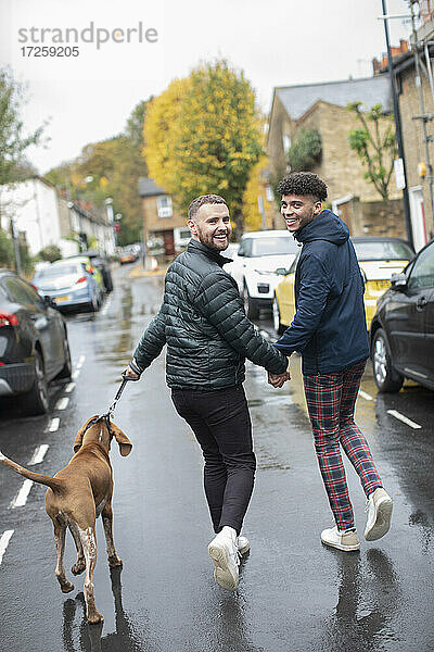 Porträt glücklich Homosexuell männliches Paar zu Fuß Hund auf nassen Herbst Straße