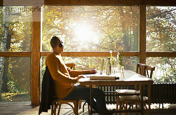 Geschäftsmann mit Kopfhörer arbeiten am Laptop in sonnigen Herbst-Café