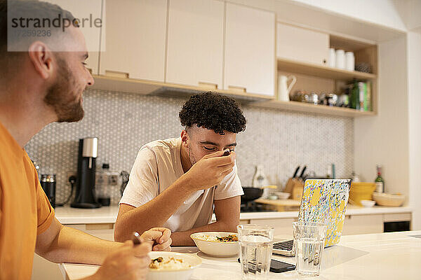 Homosexuell männliches Paar essen und mit Laptop an der Küchentheke