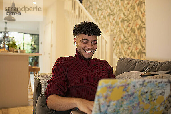 Glücklicher junger Mann mit Laptop auf dem Sofa