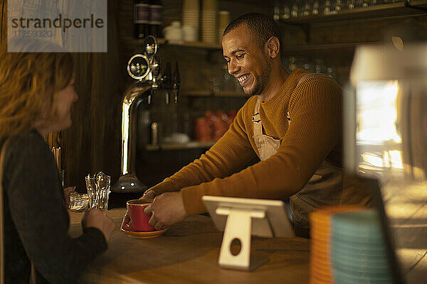 Freundlicher Barista serviert Kaffee an aufgeregte Frau am Café-Tresen