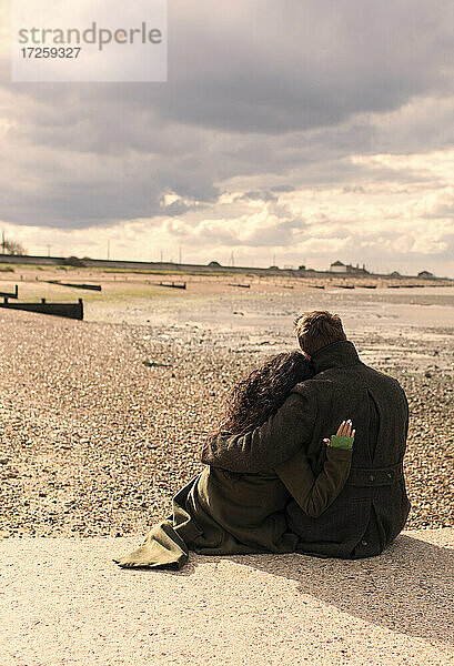 Affectionate Paar in Wintermäntel entspannen auf sonnigen ruhigen Strand
