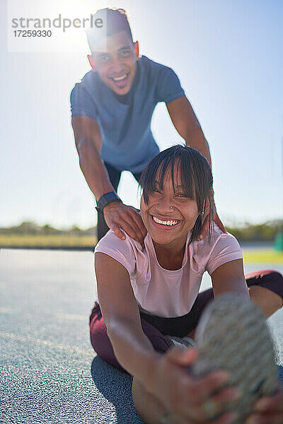 Porträt glücklich zuversichtlich  junge Läufer Stretching auf sonnigen Sportbahn