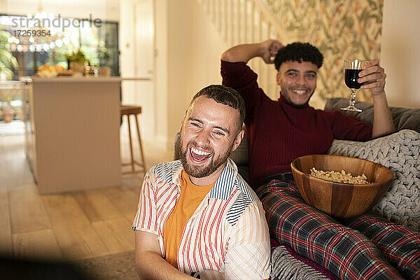 Glückliche Homosexuell männliches Paar mit Wein und Popcorn lachen und fernsehen