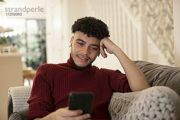 Junger Mann mit Smartphone auf dem Wohnzimmersofa