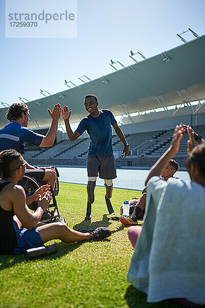 Männliche amputierte und querschnittsgelähmte Athleten beim High Fiving im sonnigen Stadion