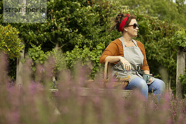 Frau mit Sonnenbrille nimmt eine Pause von der Gartenarbeit im Sommer Hinterhof