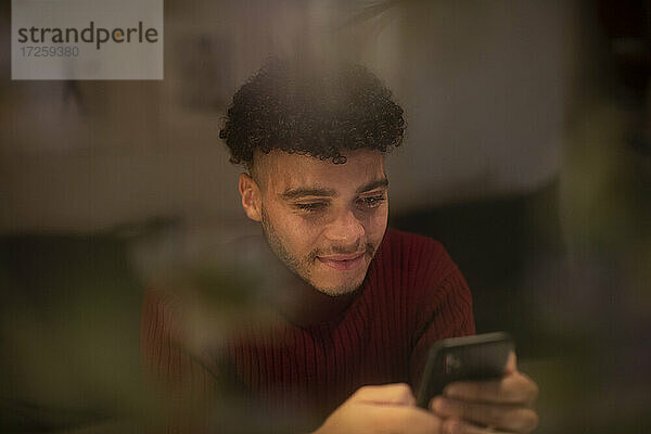 Lächelnder junger Mann mit Smartphone im Fenster